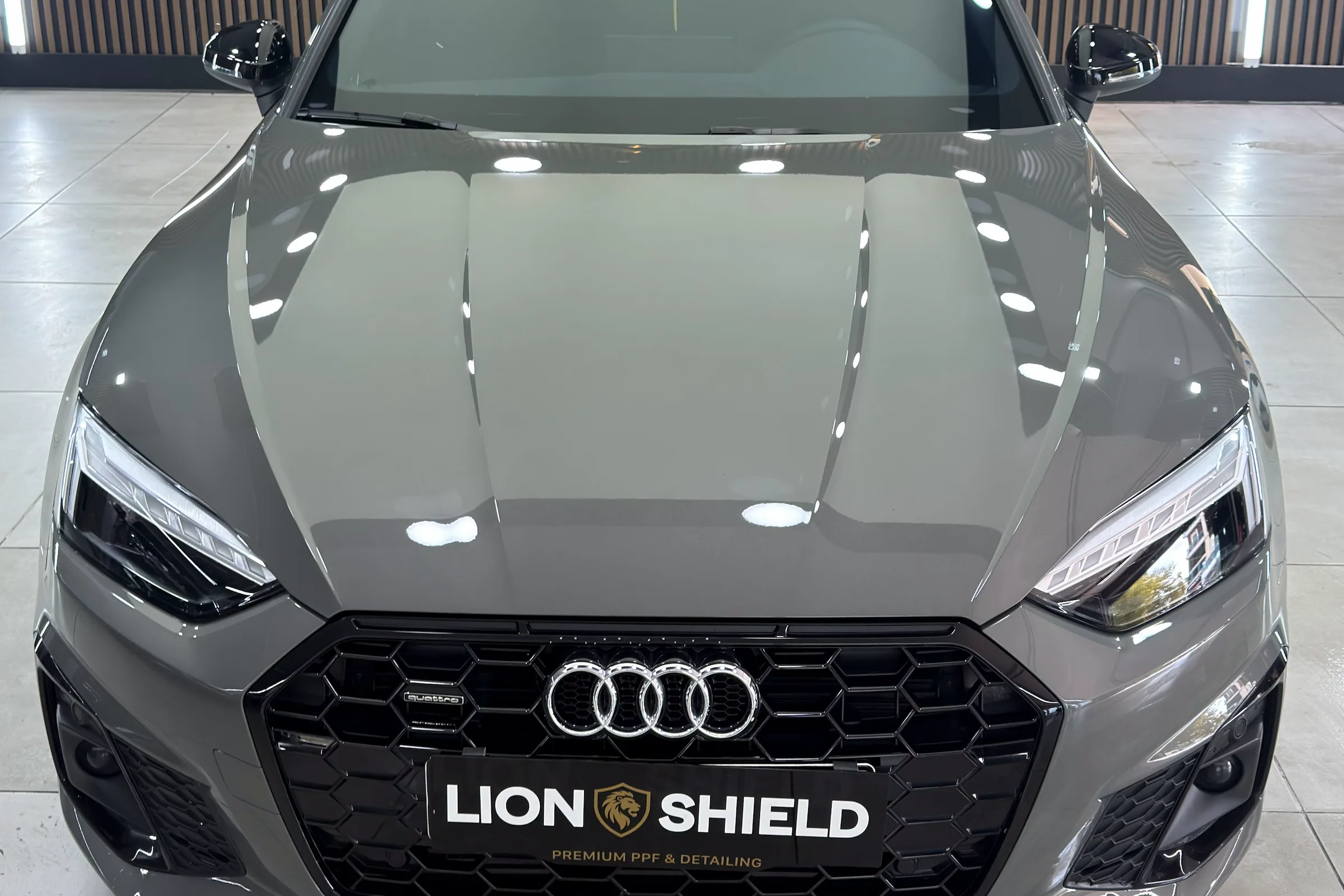 Uygulama merkezinde gri Audi A5’in kaputunda tavan ışıklarının yansıması