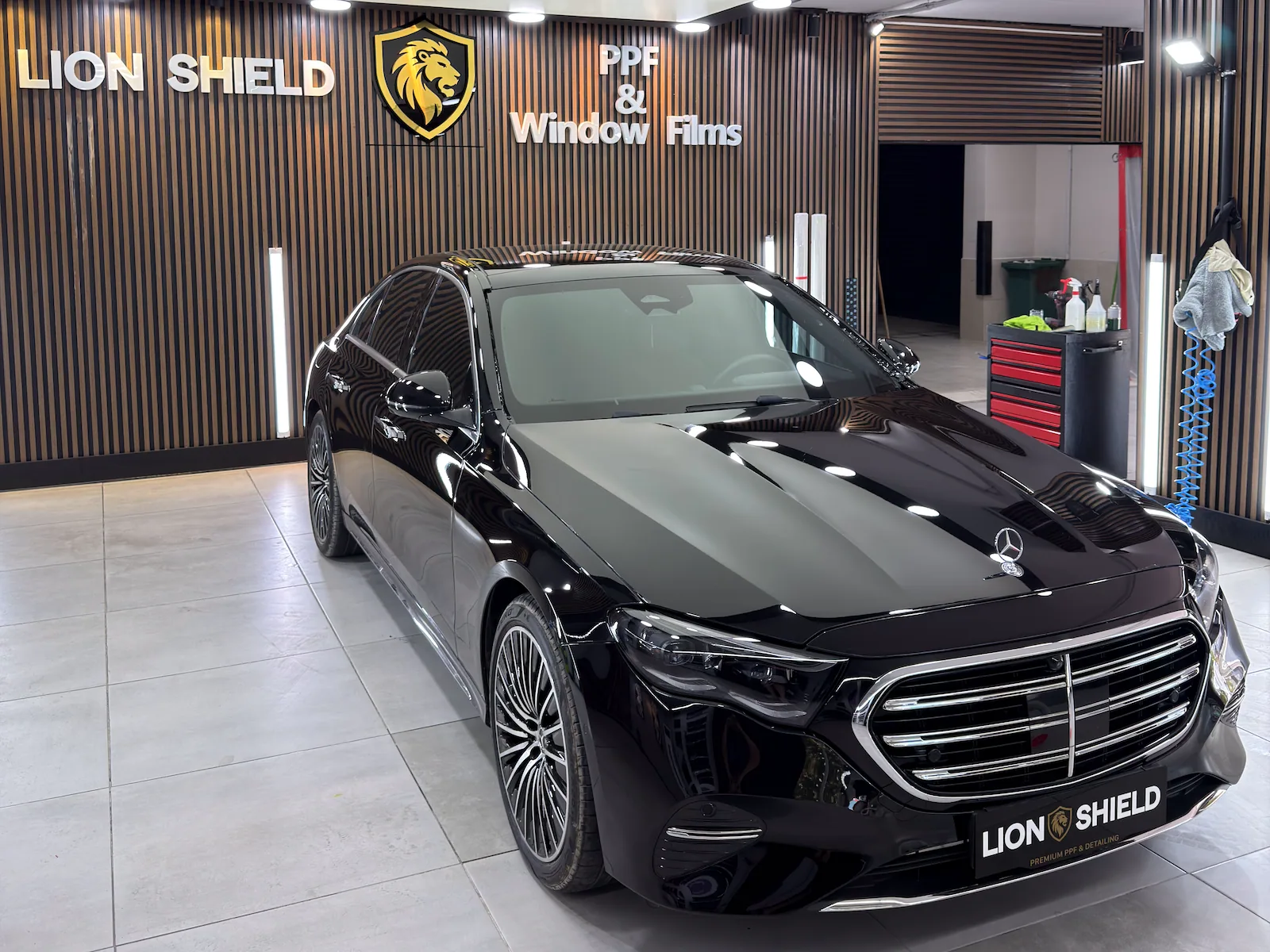 Uygulama merkezinde siyah Mercedes-Benz sedan, kaputunda tavan ışıklarının yansıması