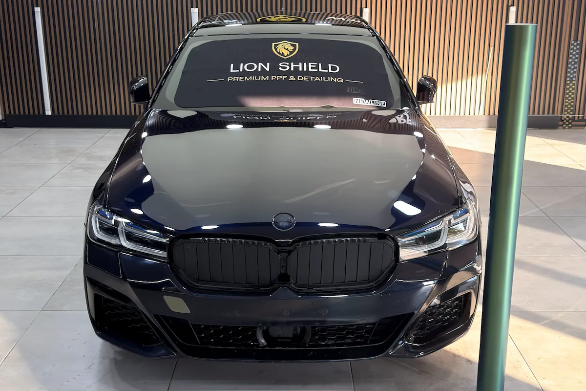 Ön ızgarası sökülmüş, ön camı örtülmüş BMW ve yanında duran film rulosu